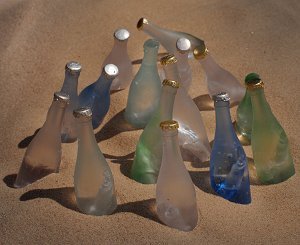 A group of various coloured bottles, cluster together in the sand...